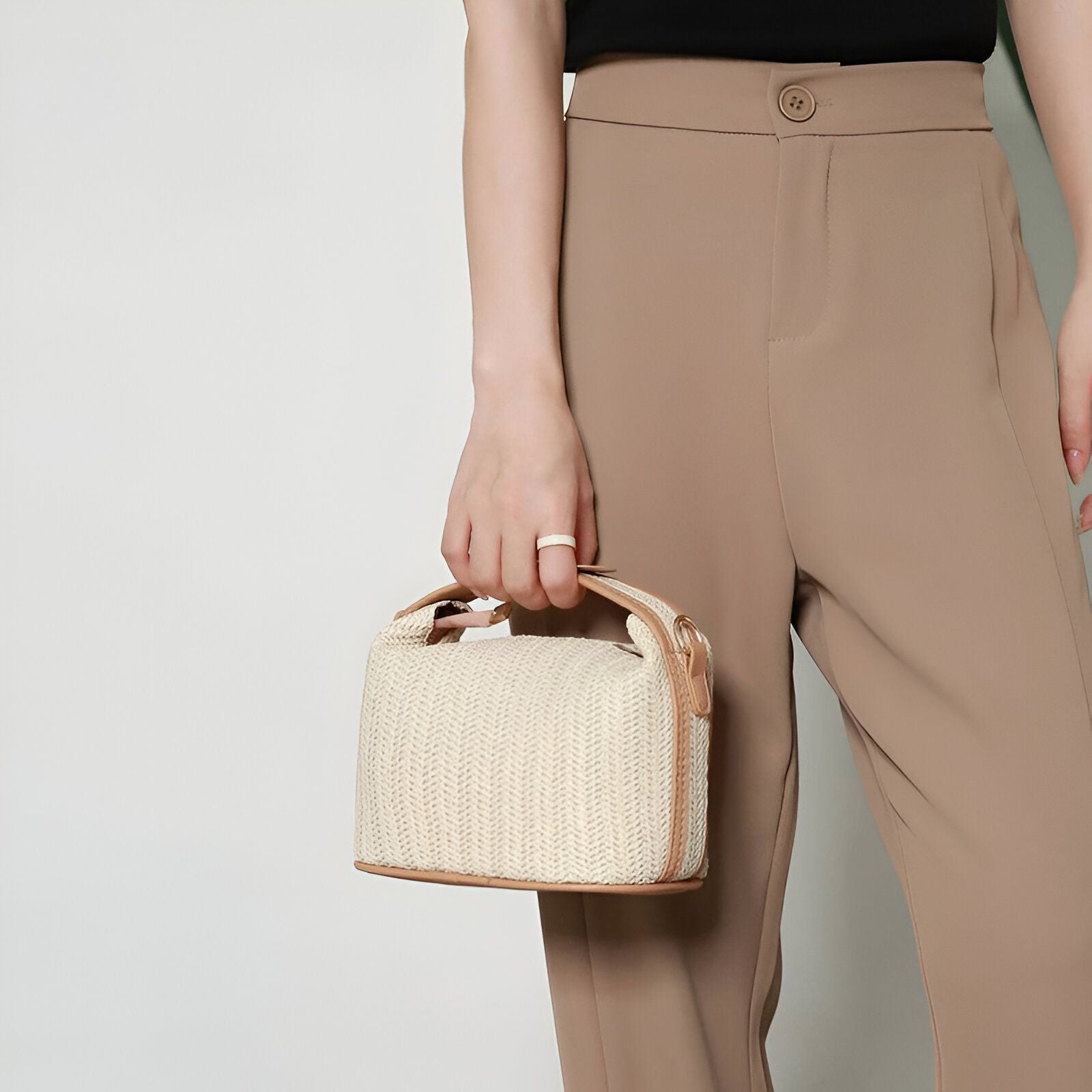 Un sac à main en paille beige porté par une femme portant un pantalon beige.