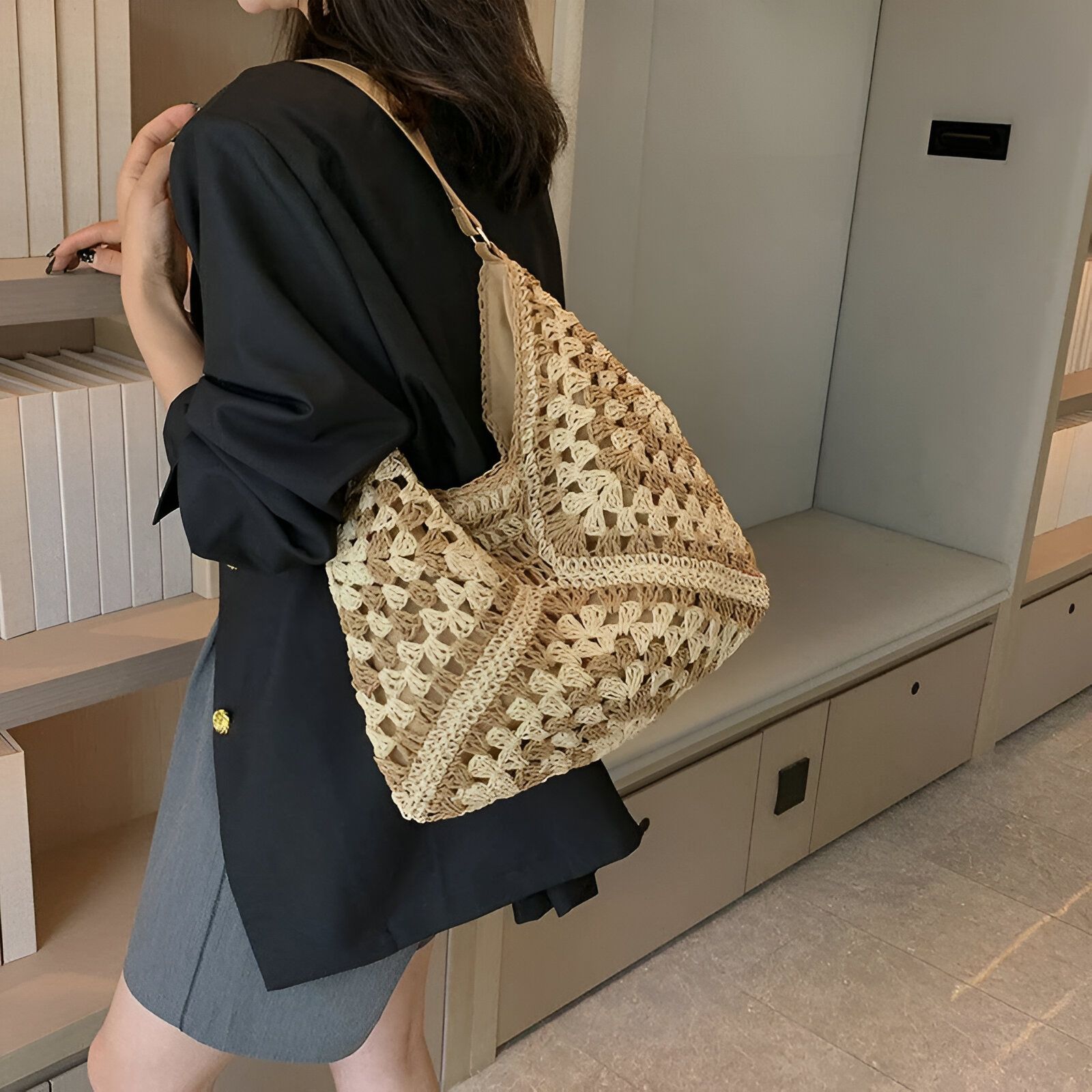 Une femme portant un sac à main en osier tressé beige et marron.  Le sac est grand et rectangulaire avec une bandoulière.