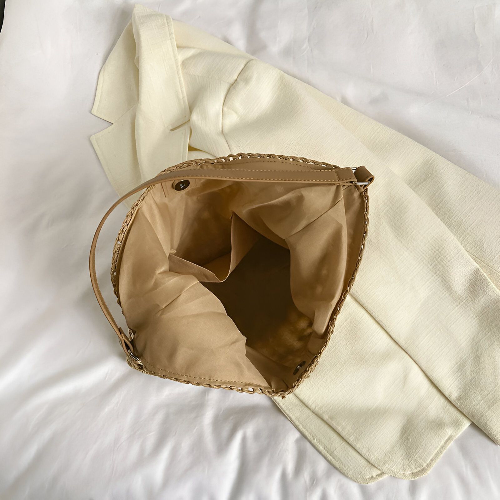 Sac à main en paille beige ouvert, montrant l'intérieur.  Il a une poche intérieure et une fermeture à bouton.