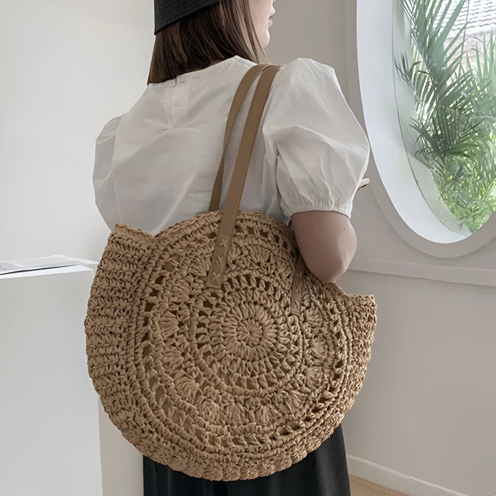 Une femme portant un grand sac à main rond en paille tressée avec des anses en cuir.