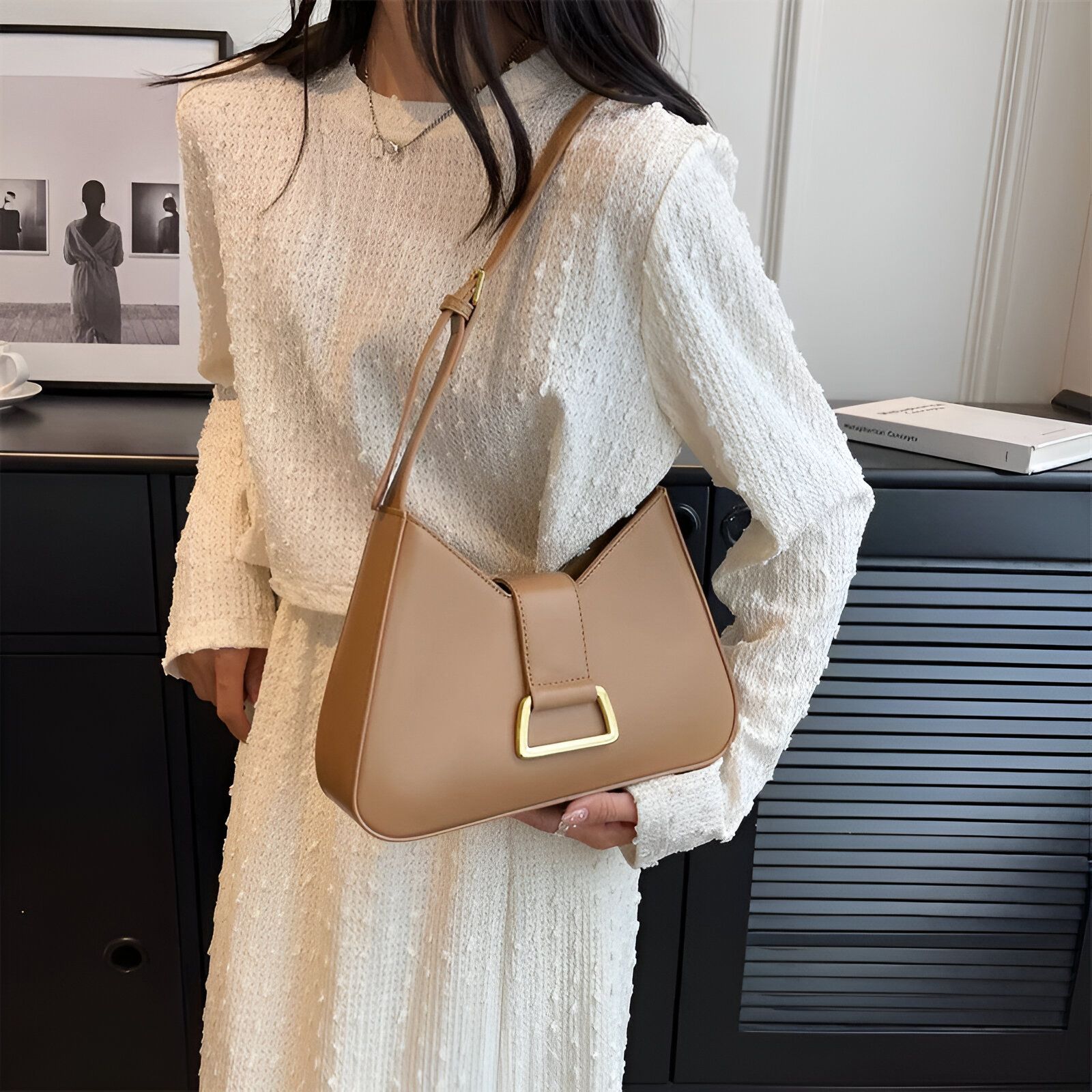 Une femme portant une robe blanche et un sac à main marron clair en forme de demi-lune avec une boucle dorée.