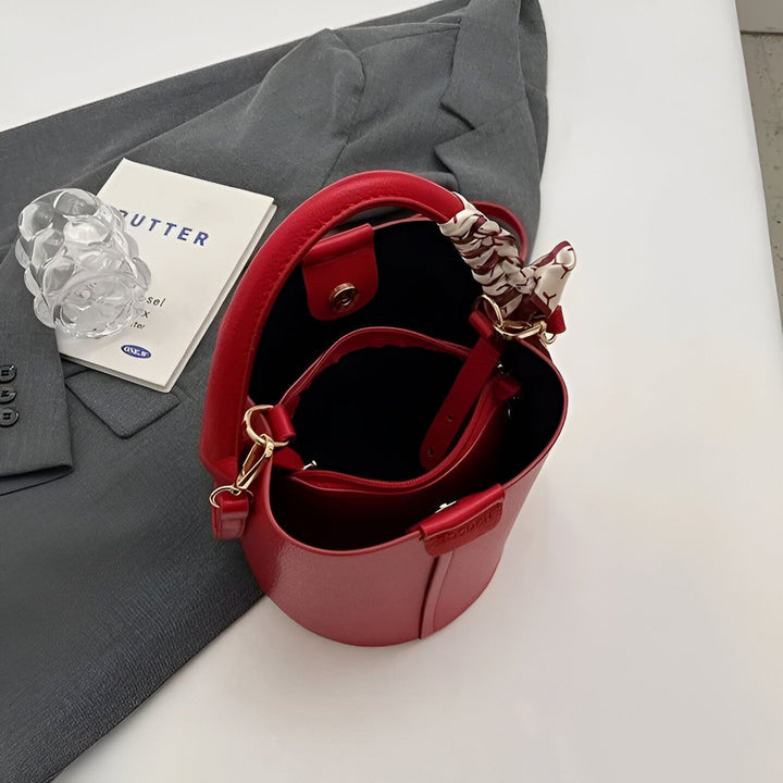 Sac seau rouge orné d'un foulard, posé sur un blazer gris., 46194006720736,46194006753504