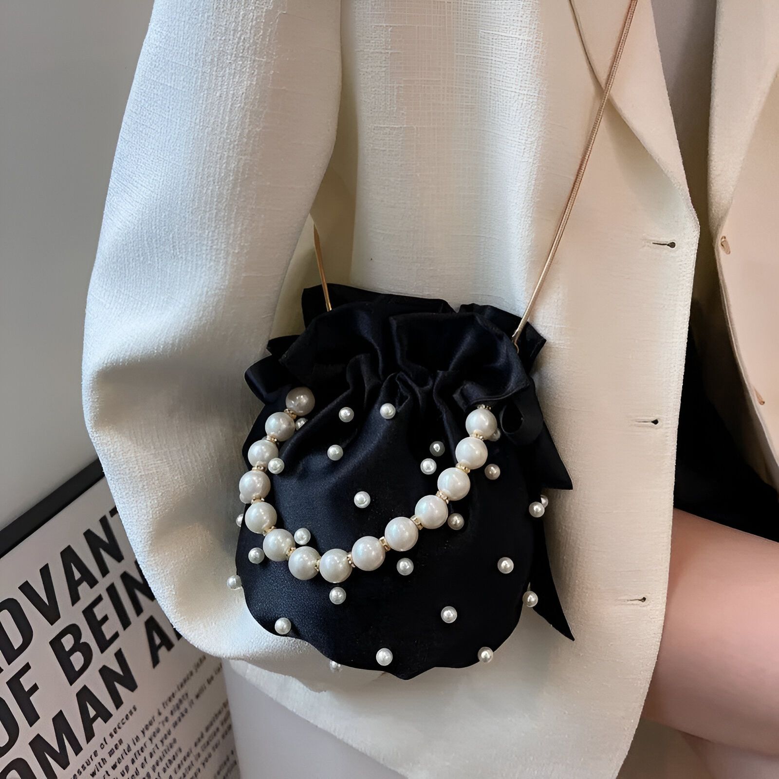 Un sac à main noir en satin avec une chaîne dorée et des perles blanches.