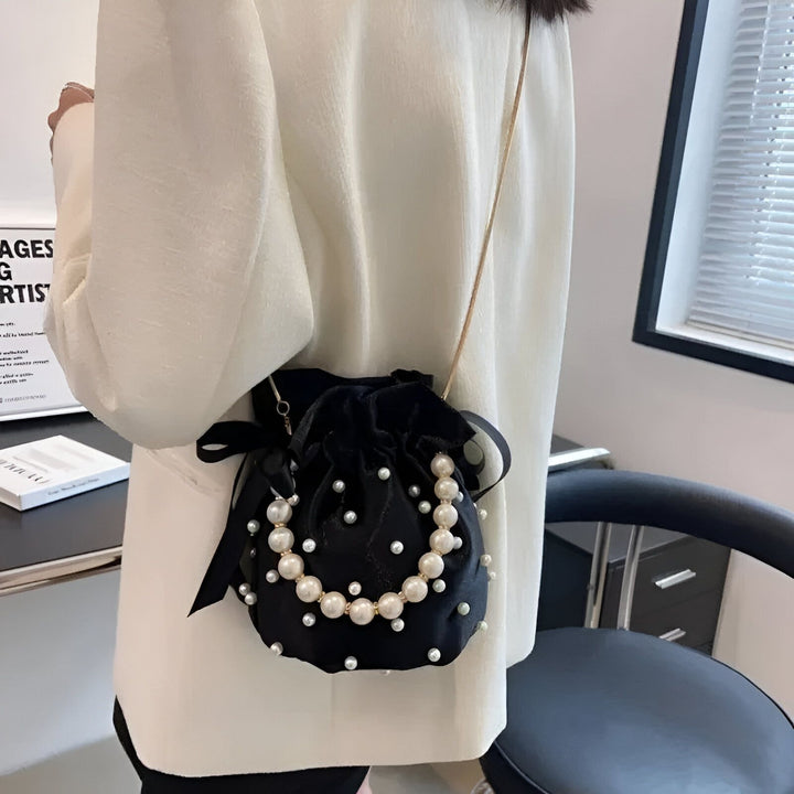 Sac pochette noir en velours orné de perles blanches, porté par une personne., 46194007572704