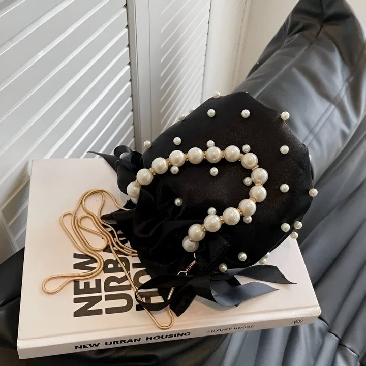 Sac noir orné de perles posé sur un livre, avec chaîne dorée., 46194007572704