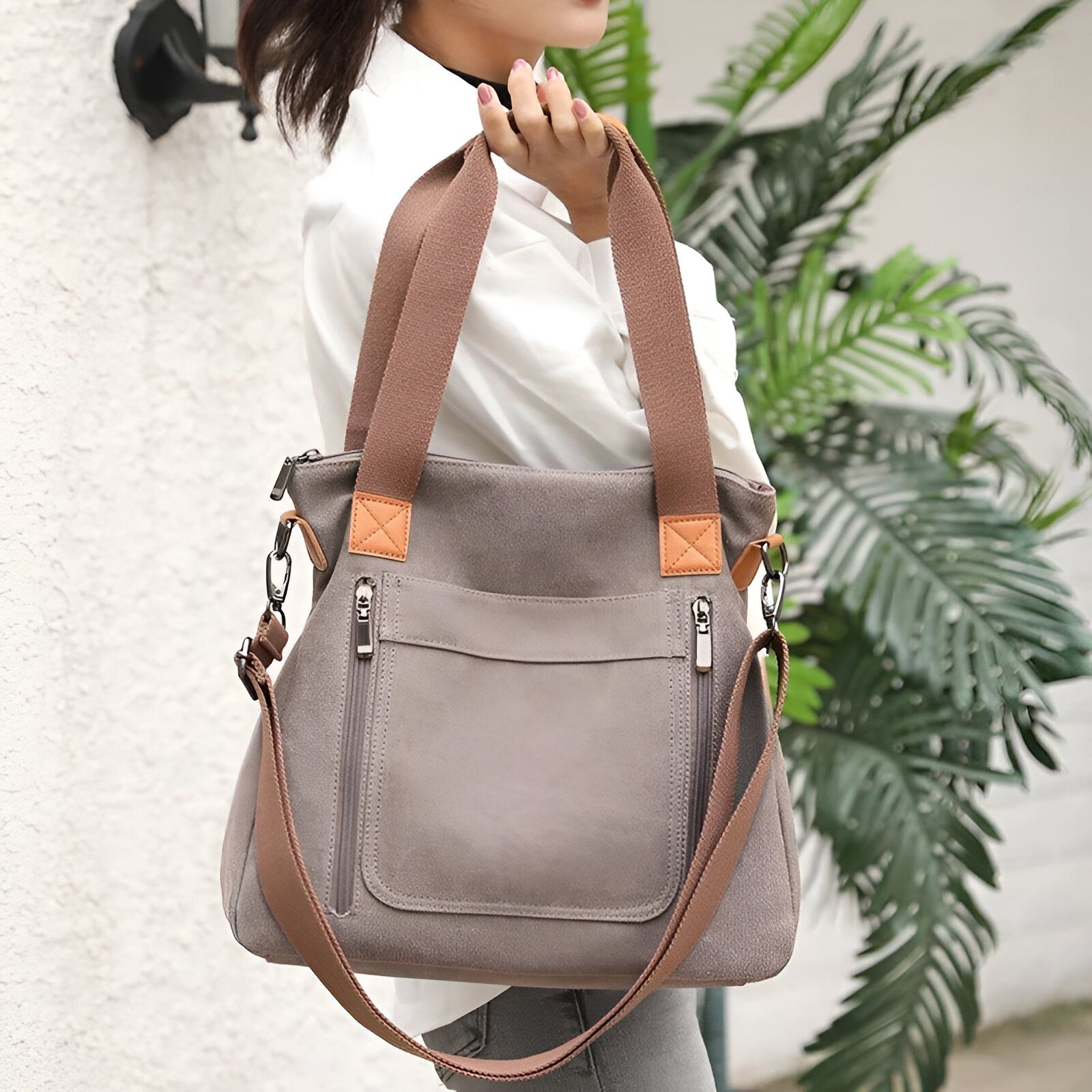 Un grand sac à main gris en toile avec des accents en cuir marron, porté par une femme.