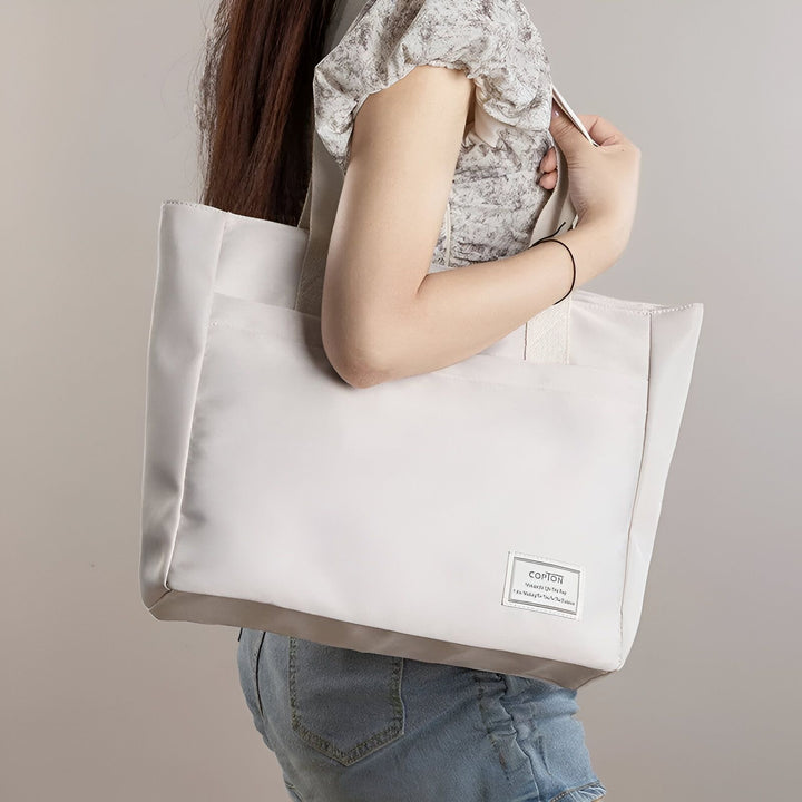 Femme portant un sac tote bag gris clair avec étiquette., 46193955471584,46193955504352,46193955537120