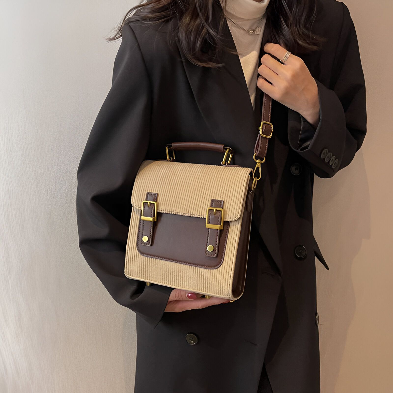 Une femme portant un sac à main en bandoulière beige avec des détails en cuir marron. Le sac a une fermeture à boucle et une poche avant.