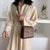 Une femme portant une robe beige et un sac à main marron.