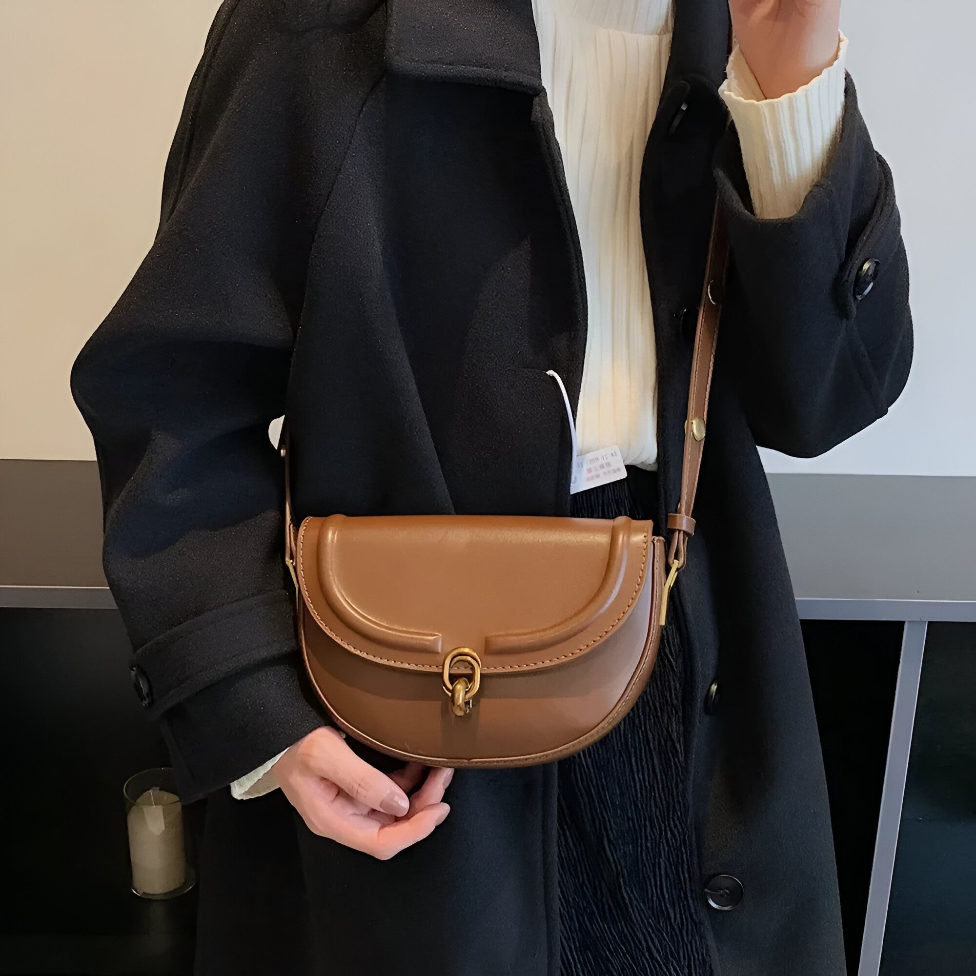 Un sac à main en cuir brun porté en bandoulière par une femme portant un manteau noir.