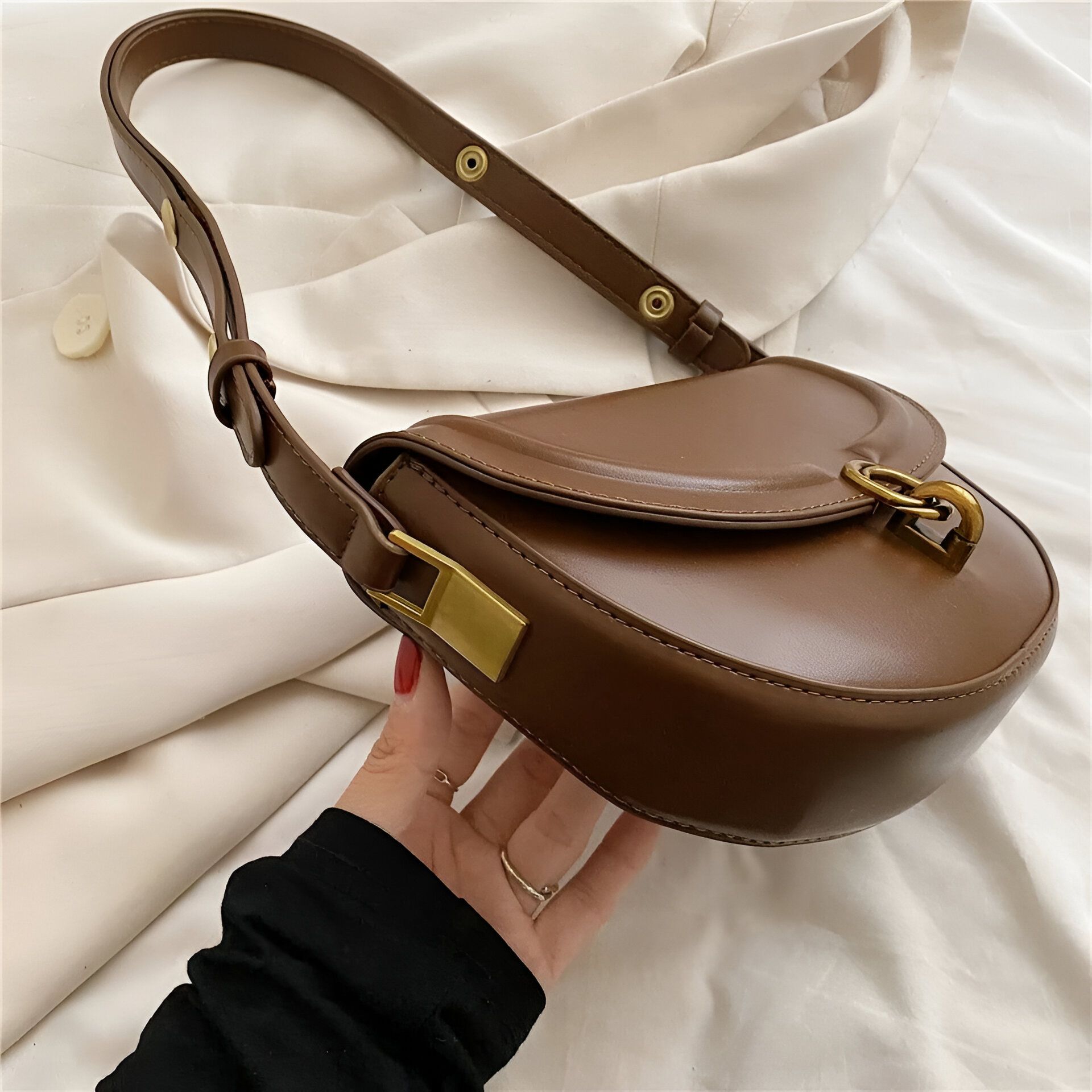 Un sac à main marron en cuir avec une bandoulière. Le sac est fermé par un fermoir doré.