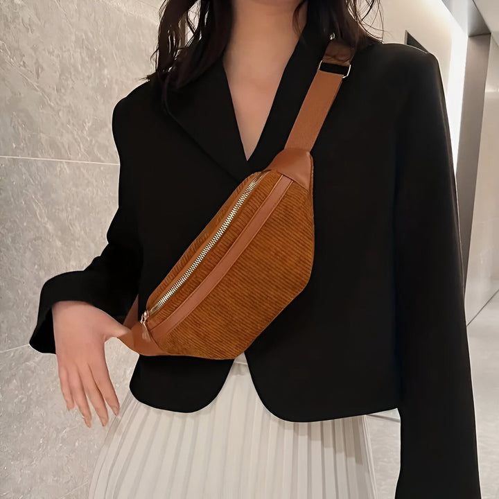 Femme portant un sac banane marron en velours côtelé en bandoulière, avec un blazer noir et une jupe blanche plissée., 46194025726176,46194025758944,46194025791712