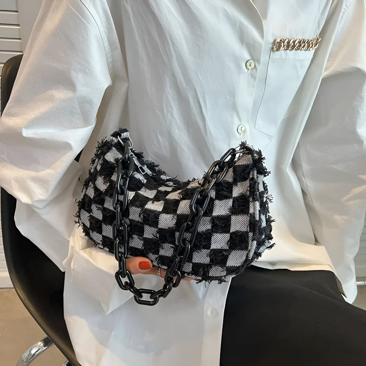 Sac à main à damier noir et blanc avec chaînes épaisses, tenu par une personne en chemise blanche., 46193995612384,46193995645152
