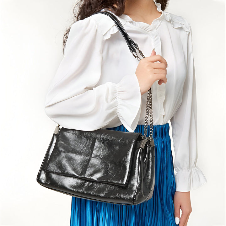 Sac à bandoulière noir matelassé avec chaîne, porté sur une épaule., 46193950523616,46193950556384