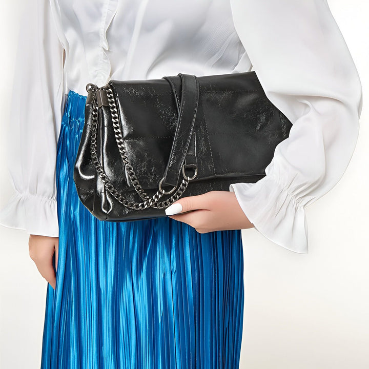Sac pochette noir chaîne métal porté avec jupe plissée bleue et chemisier blanc., 46193950523616,46193950556384