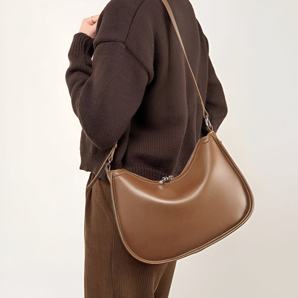 Sac bandoulière en cuir marron porté épaule, forme courbée., 46193853104352