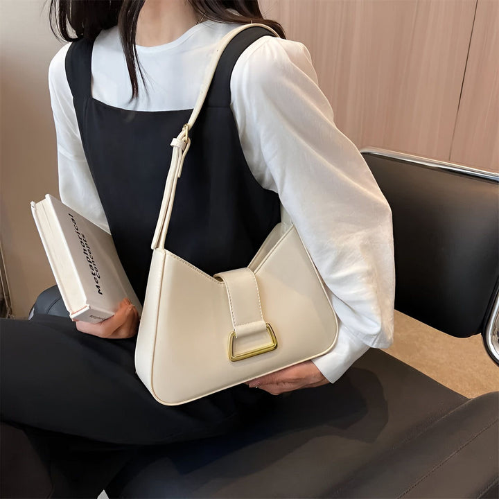 Sac à main beige sur l'épaule avec boucle dorée porté par une femme lisant un livre., 46193872797920,46193872830688,46193872863456,46193872896224