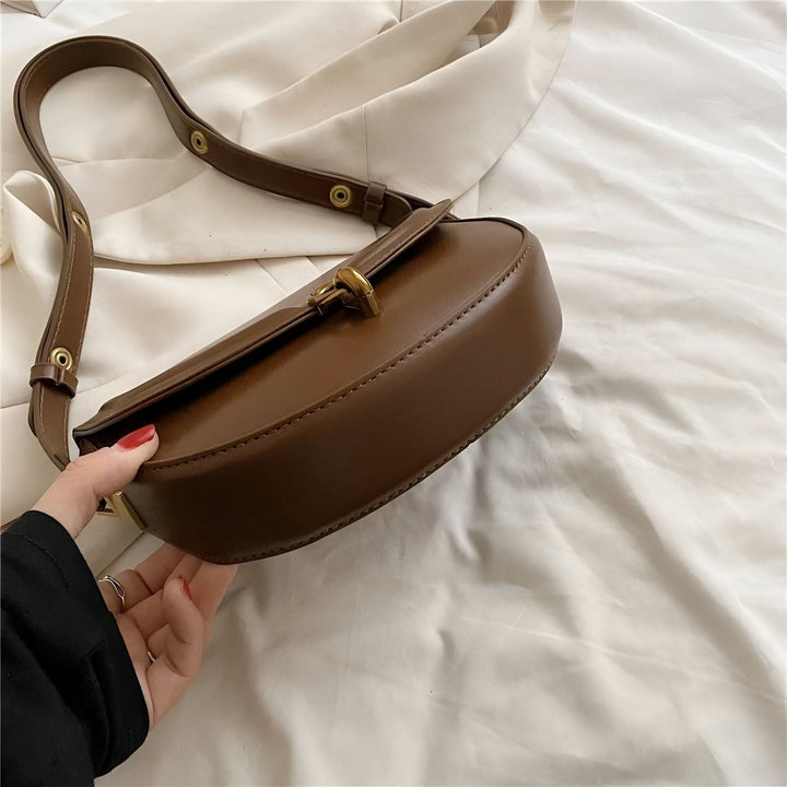 Main tenant un sac à bandoulière en cuir marron avec bandoulière fine et boucle dorée., 46194026283232,46194026316000,46194026348768,46194026381536