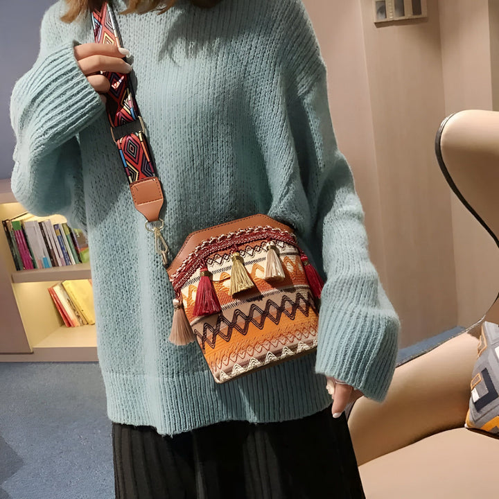 Sac à bandoulière brodé avec motifs ethniques, pompons et sangle colorée, porté sur un pull bleu., 46193925193952,46193925226720,46193925259488,46193925292256