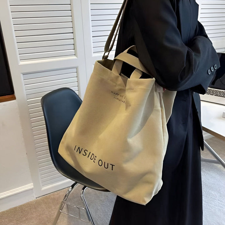 Sac tote bag beige avec inscription "INSIDE OUT", porté sur l'épaule par une personne en noir., 46193896751328,46193896784096