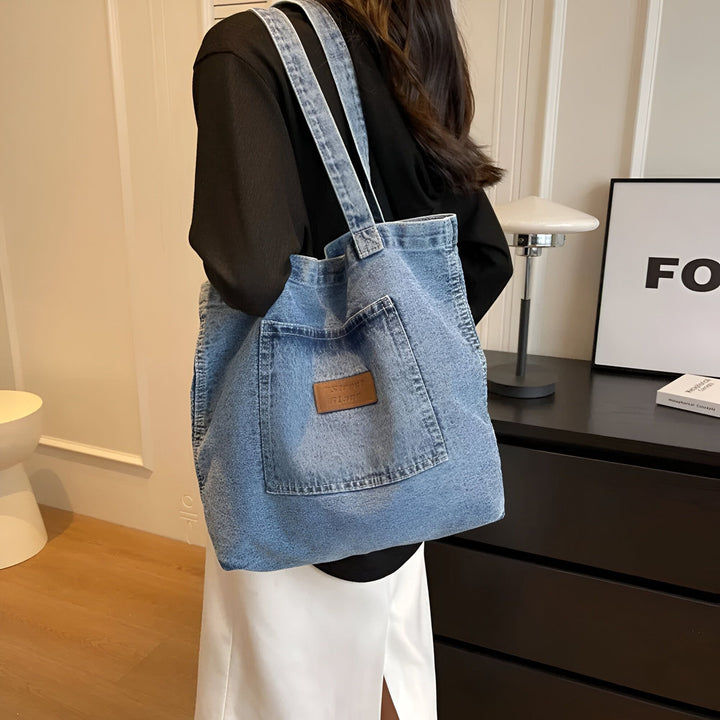 Personne portant un sac cabas en jean bleu délavé avec poche avant et étiquette cuir., 46193991942368,46193991975136