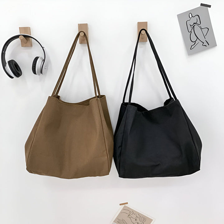 Deux sacs cabas marron et noir suspendus sur un mur blanc., 46193893048544,46193893081312