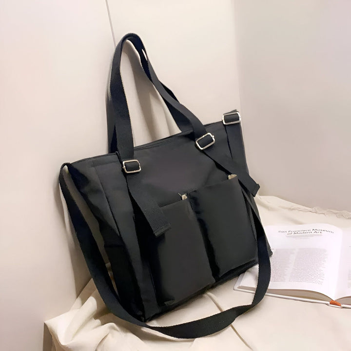 Sac cabas noir avec poches et bandoulière posé à côté d'un livre ouvert., 46193874796768,46193874829536,46193874862304