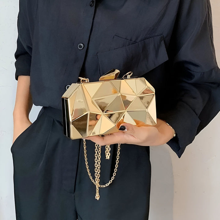 Sac pochette doré géométrique avec chaîne, tenu par une personne en noir., 46194013569248,46194013602016,46194013634784