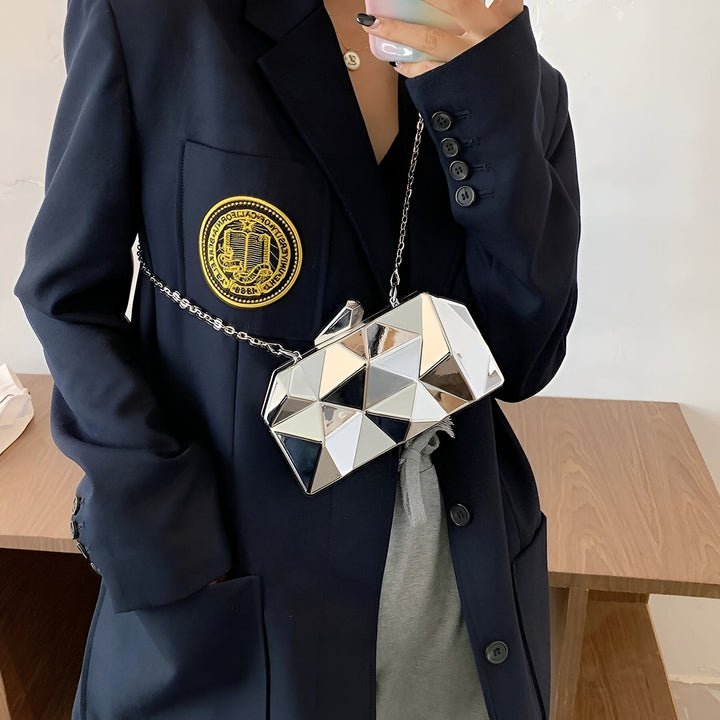 Sac pochette géométrique miroir argenté et or avec chaîne porté sur un blazer marine., 46194013569248,46194013602016,46194013634784