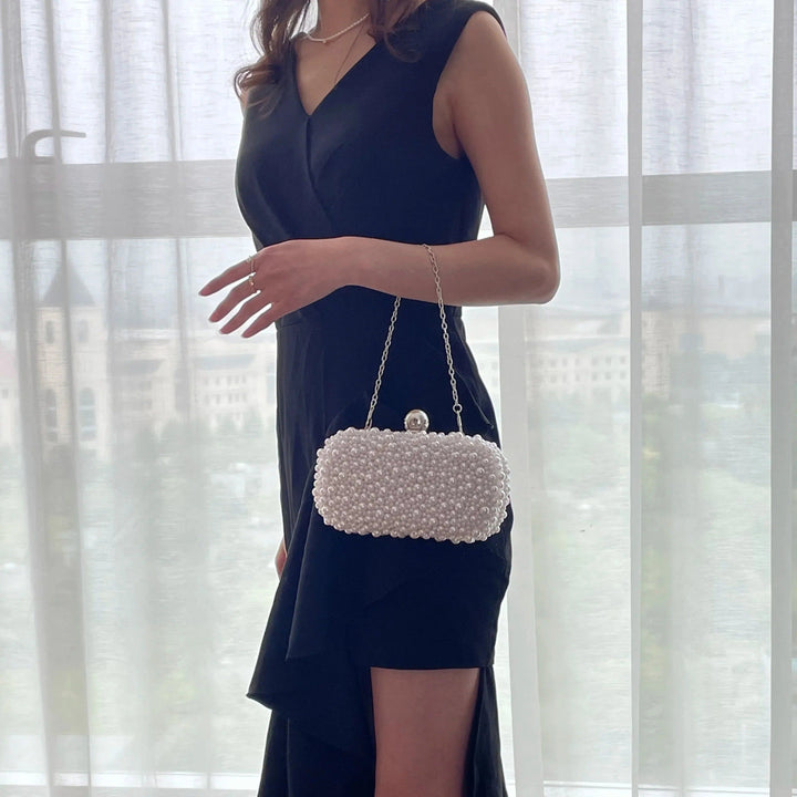 Femme en robe noire tenant une pochette blanche ornée de perles., 46193928896736,46193928929504