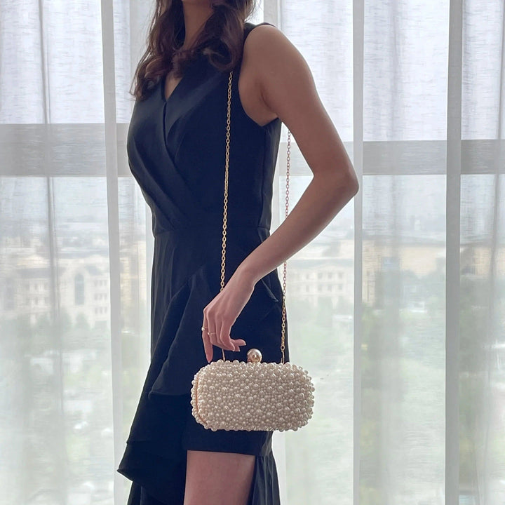 Femme en robe noire et pochette blanche perlée à chaîne dorée., 46193928896736,46193928929504