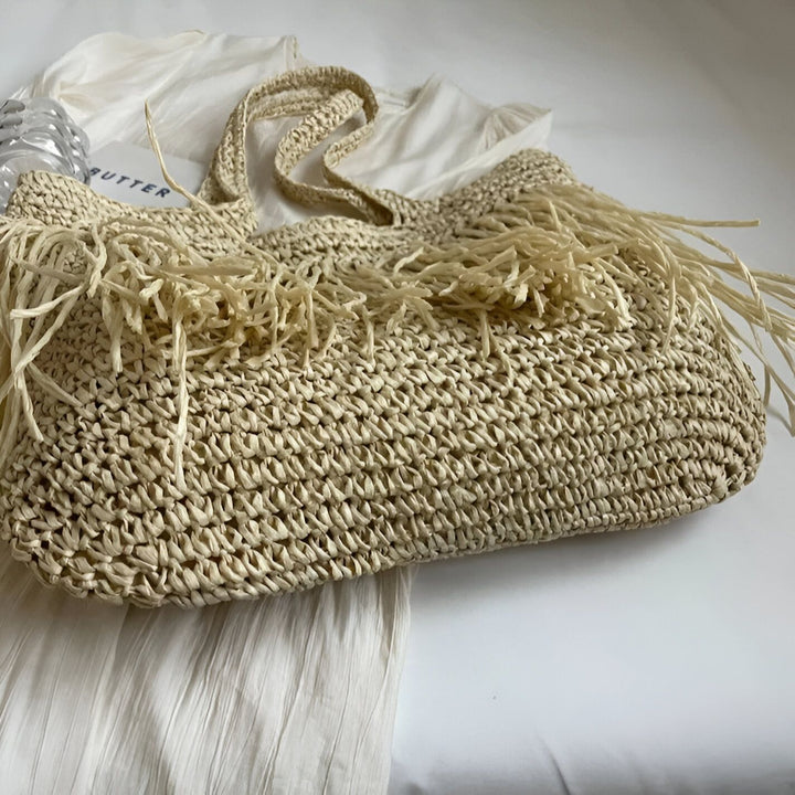 Sac cabas en paille beige avec franges et anses, posé sur un tissu blanc., 46193922965728,46193922998496