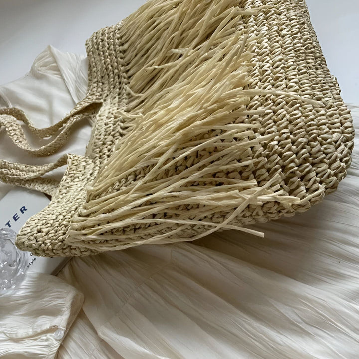 Sac en paille tressée à franges posé sur une robe blanche froissée., 46193922965728,46193922998496