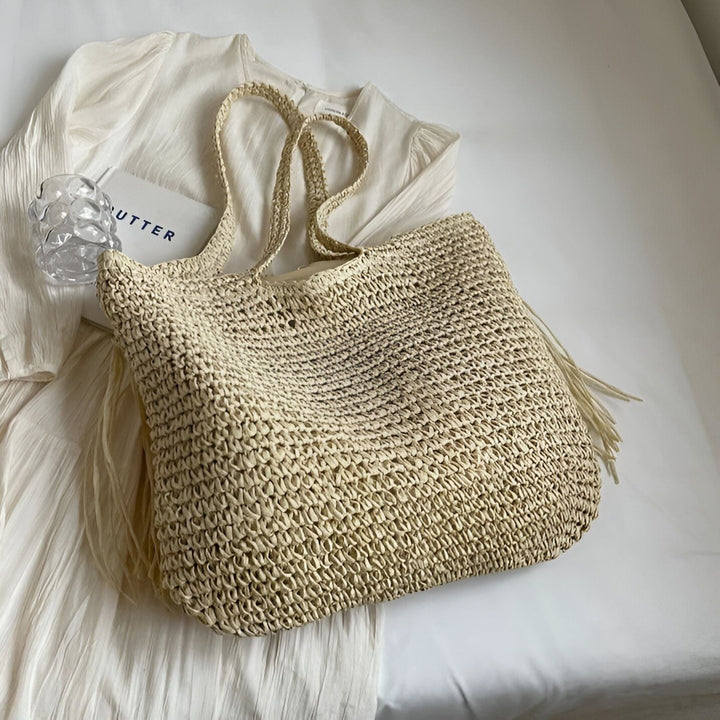 Sac cabas en paille posé sur une blouse blanche à côté d'un livre et d'un verre., 46193922965728,46193922998496