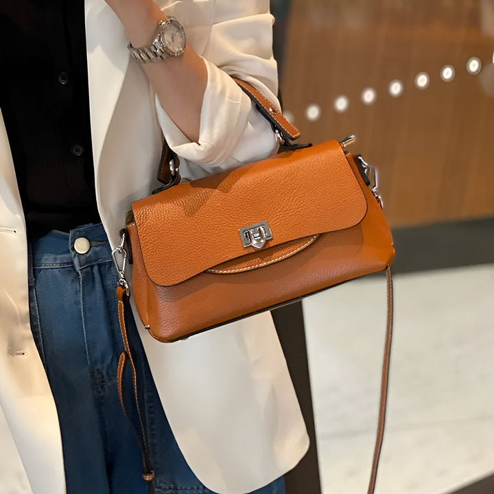 Personne portant un sac à main marron en cuir grainé à rabat et fermoir métal., 46193852252384