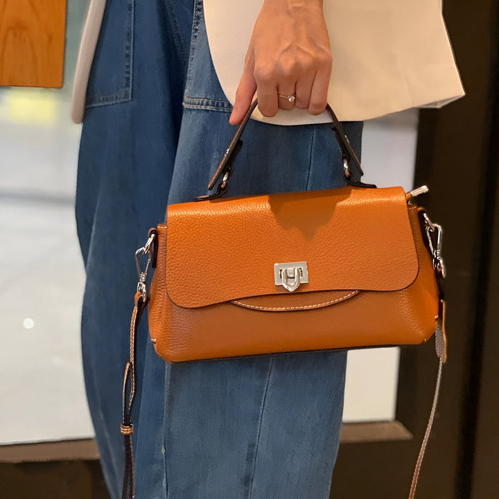 Sac à main en cuir texturé couleur cognac avec rabat et anse, porté par une femme., 46193852252384