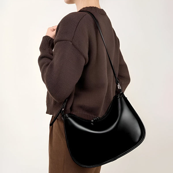 Sac hobo noir brillant porté sur l'épaule par une personne en pull marron., 46193867751648