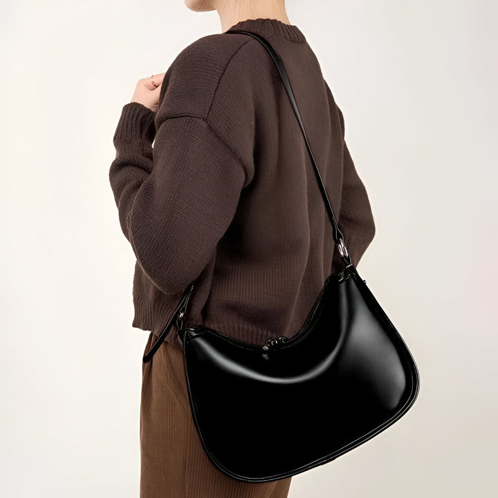 Sac hobo noir brillant porté sur l'épaule par une personne en pull marron., 46193867751648