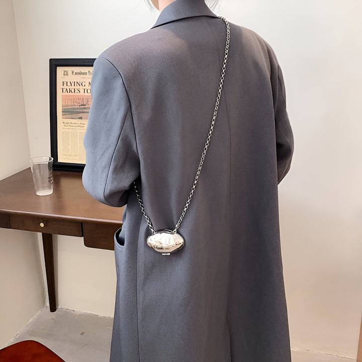 Personne en manteau gris vue de dos avec un petit sac ovale argenté porté en bandoulière., 46193973788896,46193973821664