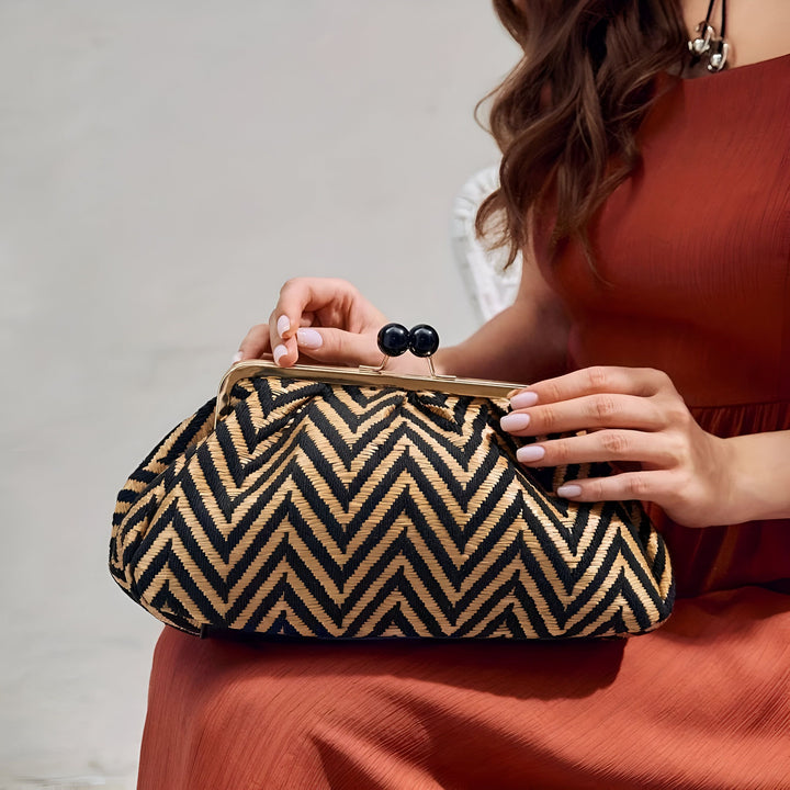 Femme tenant une pochette à motif zigzag noir et beige avec fermoir doré, 46194023006432