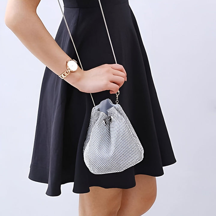 Femme en robe noire tenant une pochette argentée scintillante., 46194028544224,46194028576992,46194028609760