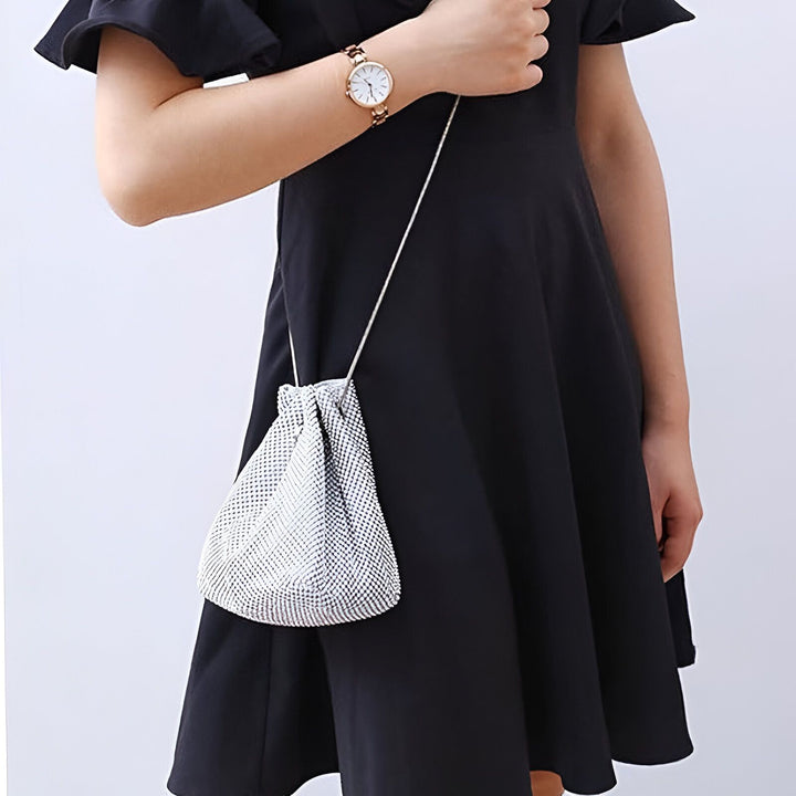 Femme en robe noire tenant un petit sac blanc scintillant avec un cordon et une montre., 46194028544224,46194028576992,46194028609760